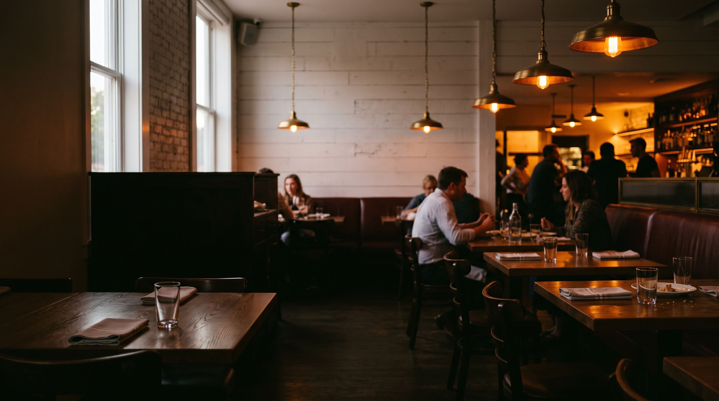 The dining room at dusk, tables glowing under brass pendant lamps.